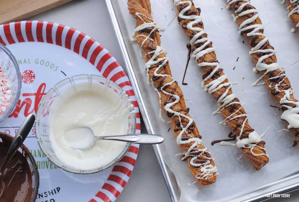 White chocolate in bowl drizzled on churros on baking sheet